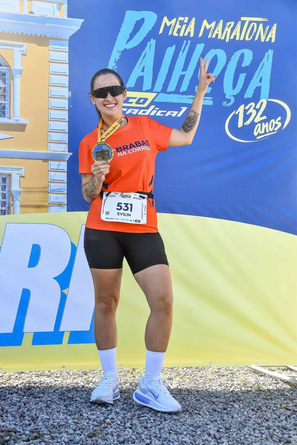 Atleta exibe a medalha de participação diante do painel da prova